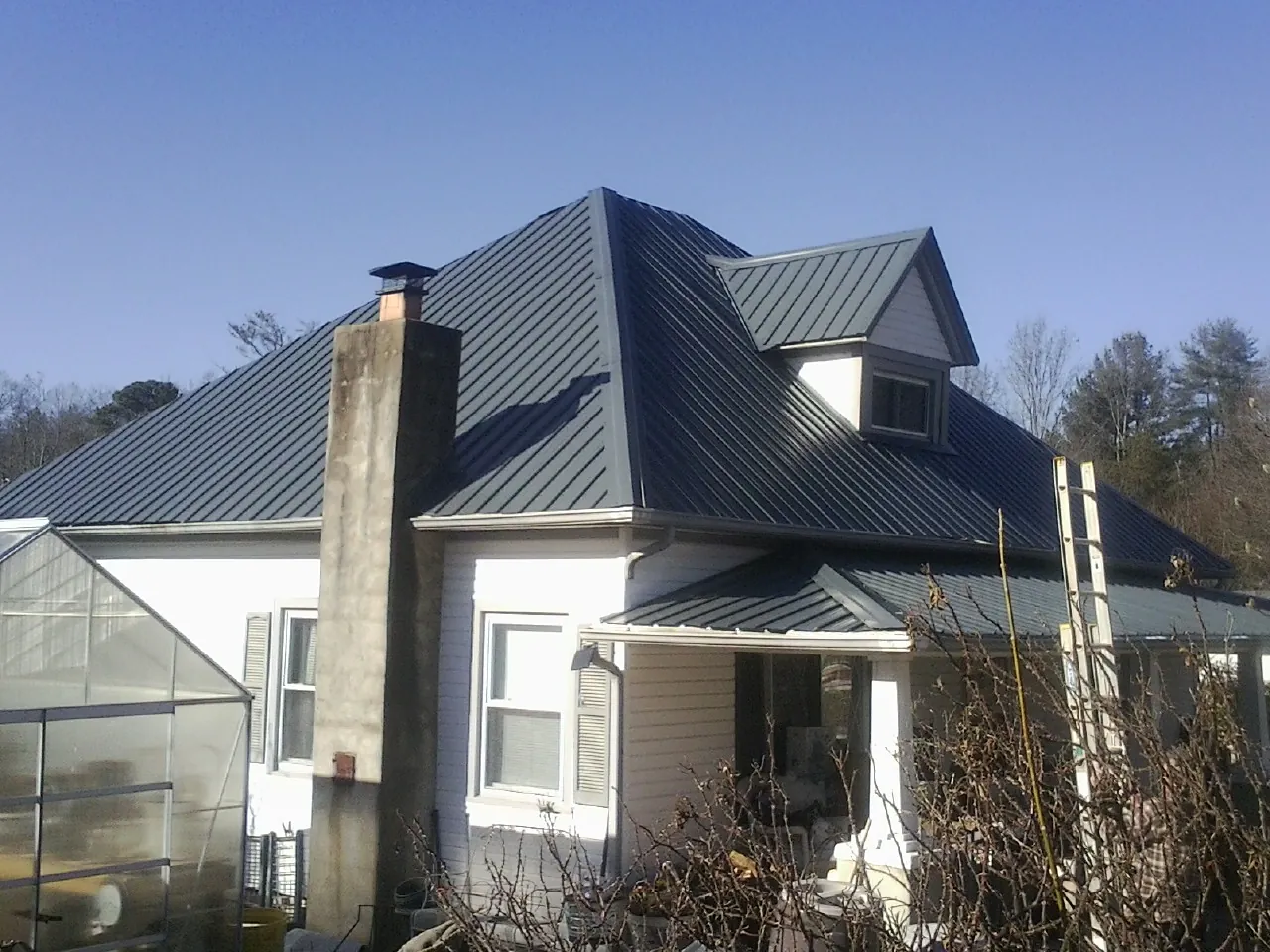 Dark blue standing seam metal roof on a white farmhouse with dormer — Slate & Tile Roof Repair by Roofing Brothers in Zenia