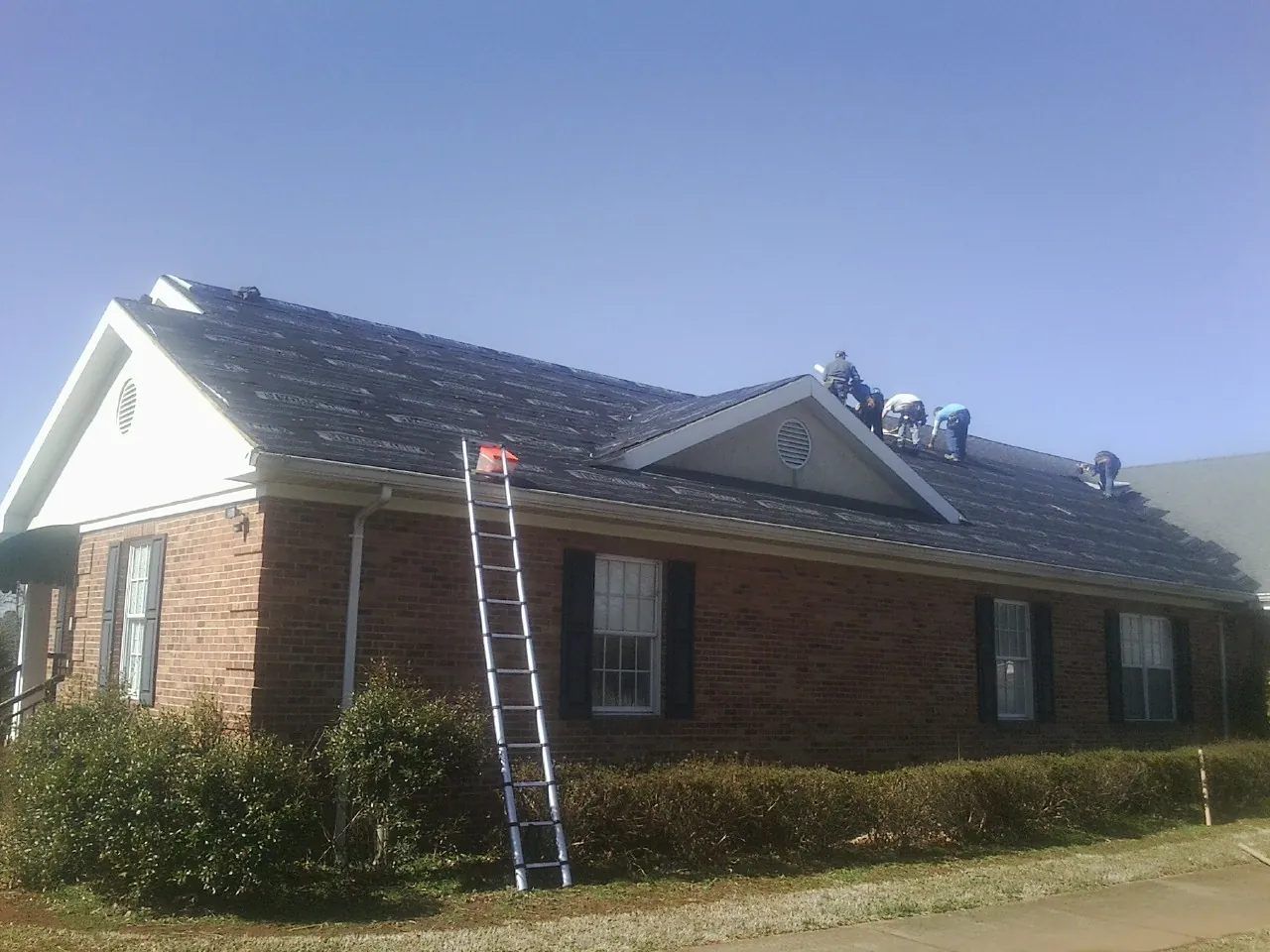 Crew tearing shingles off a brick ranch roof with a ladder set — Metal Roof Repair work by our crew in Zenia