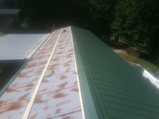 Old rusted panels beside newly installed green metal roofing — Wind Damage Roof Repair by Roofing Brothers in Zenia