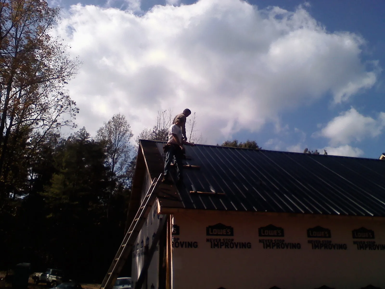Roofer fastening dark metal panels high against a cloudy sky, from a Roof Inspection job in Zenia