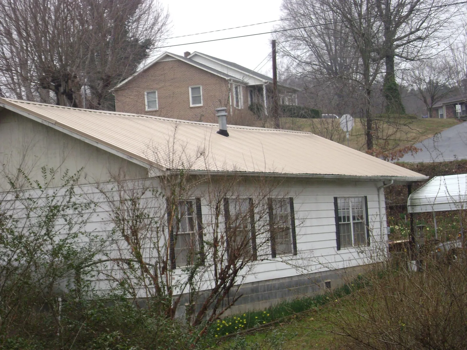 Tan metal roof on a white sided house set into a hillside — Commercial Roofing by Roofing Brothers in Zenia